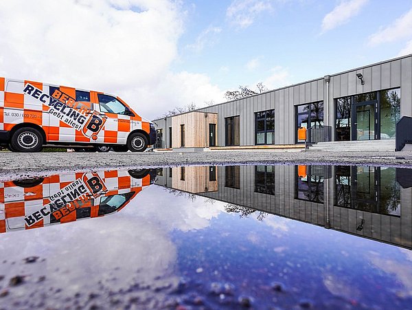 Foto, Oranger Recycling-Transporter mit Schriftzug 'Berlin Recycling' vor modernem Gebäude, Spiegelung im Wasserpfütze