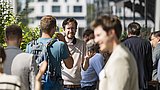 Foto, eine Gruppe von Menschen unterhält sich im Freien, umgeben von Grün, in einer modernen städtischen Umgebung, einige davon in Geschäftskleidung.