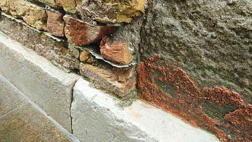 Foto, Nahaufnahme eines freigelegten Mauerwerks mit sichtbaren Ziegelsteinen und Putzresten auf einem Sockel.