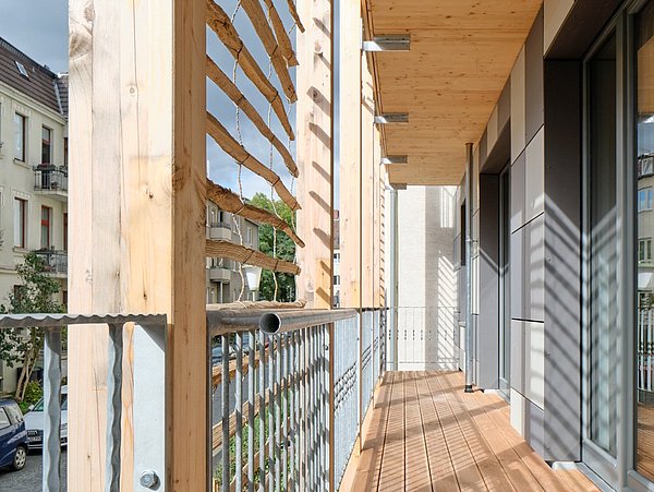 Foto, Balkon mit Holzgeländer und Holzboden an einem modernen Gebäude mit Blick auf eine Straße und Nachbarhäuser