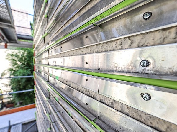 Foto, Metallstreben mit grünen Kunststoffrohren an einer Betonwand befestigt, Teil einer Bauinstallation