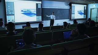Foto, eine Dozentin präsentiert architektonische Inhalte in einem Hörsaal.