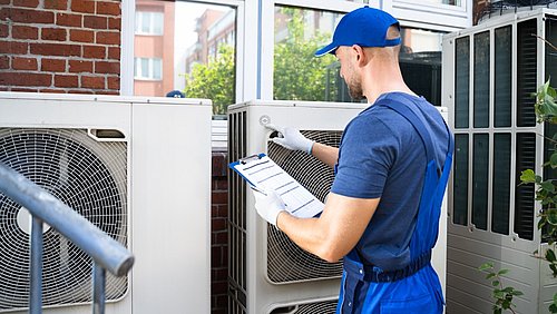 Foto, ein Techniker mit Klemmbrett inspiziert eine Wärmepumpe.