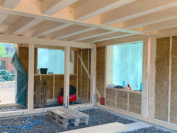 Foto, Innenansicht eines Rohbaus mit Holzrahmen und Strohdämmung, Boden mit Schaumglasschotter und Paletten