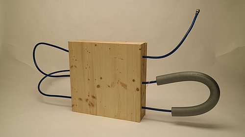 Foto, Bauelement aus Holz, durch welches schlaufenförmig ein Schlauch läuft.