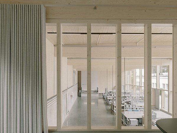 Foto, Vorhang mit feiner Struktur links, rechts dahinter helle, moderne Arbeitsräume mit großen Fenstern und Tischen.