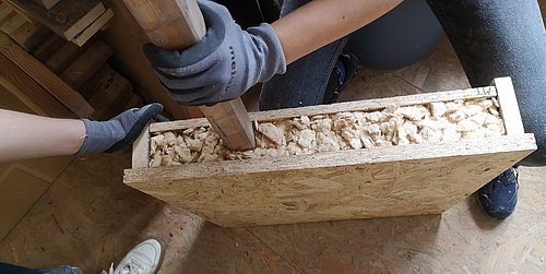 Foto, Nahaufnahme von zwei Personen, die ein Bauelement mit Dämmmaterial füllen.