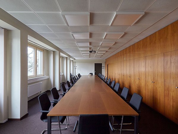 Foto, großes Konferenzraum mit großem Tisch, Stühlen und Holzvertäfelung auf der rechten Seite des Raums.