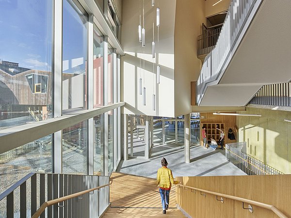 Foto, Person in gelber Jacke geht Treppe in einem modernen, hellen Gebäude mit großen Fenstern und hängenden Leuchten hinunter
