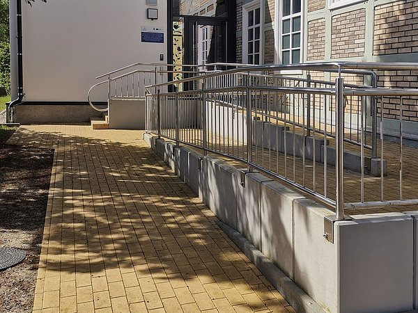 Foto, Barrierefreie Rampe mit Edelstahlgeländer an einem Fachwerkgebäude mit weißen Fensterrahmen