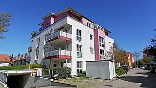 Foto, Mehrstöckiges Wohngebäude mit Balkonen und roten Akzenten an einem sonnigen Tag