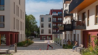 Foto, Innenhof zwischen modernen Mehrfamilienhäusern. In der Mitte läuft ein Kind hinter einem Ball.