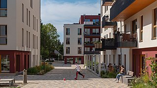 Foto, Innenhof zwischen modernen Mehrfamilienhäusern. In der Mitte läuft ein Kind hinter einem Ball.