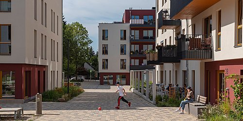 Foto, Innenhof zwischen modernen Mehrfamilienhäusern. In der Mitte läuft ein Kind hinter einem Ball.