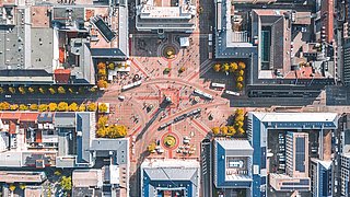 Foto, Luftaufnahme eines großen, sternförmigen Platzes mit mehreren Straßen, umgeben von mehrstöckigen Gebäuden und herbstlich gefärbten Bäumen.
