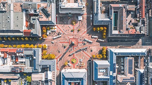 Foto, Luftaufnahme eines großen, sternförmigen Platzes mit mehreren Straßen, umgeben von mehrstöckigen Gebäuden und herbstlich gefärbten Bäumen.