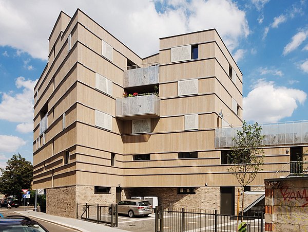 Foto, Außenansicht eines mehrstöckigen Gebäudes mit Holzfassade und zwei Balkonen. 