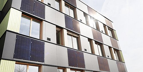 Foto, Mehrstöckiges Gebäude mit Fassadenverkleidung aus Solarpaneelen und Fenstern unter bewölktem Himmel