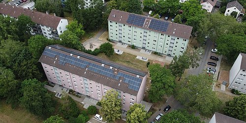 Foto, Mehrfamilienhäuser mit Solaranlagen auf den Dächern, umgeben von Bäumen und Parkplätzen in einem Wohngebiet