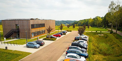 Foto, Außenaufnahme der Forschungshalle in Feuchtwangen mit einem Parkplatz in Vordergrund.