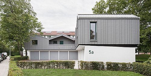 Foto, moderne Wohnhausaufstockung, gebaut auf Garagen, umgeben von Büschen und Bäumen