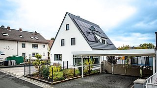 Foto, Einfamilienhaus mit Carport, Garten und Photovoltaikanlage auf dem Dach. 