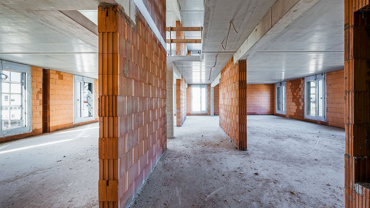Foto, Innenaufnahme eines Rohbaus. Es sind unverputzte Wände, Böden und Decken zu sehen.