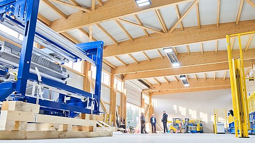 Foto, Innenansicht einer großen Industriehalle mit Holzbalkendecke, mehreren Personen und gelbem Gabelstapler