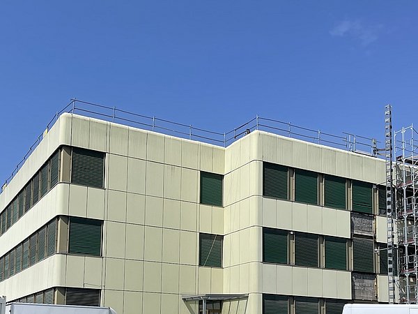 Eckgebäude mit grünen Fenstern und einem Gerüst an der Seite.