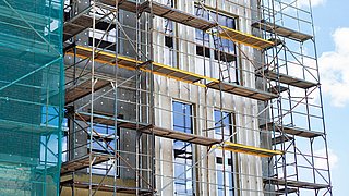 Foto, Fassade eines mehrstöckigen Gebäudes mit Gerüst und gelben Arbeitsplattformen.