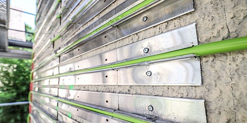 Foto, Metallstreben mit grünen Kunststoffrohren an einer Betonwand befestigt, Teil einer Bauinstallation