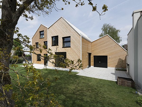Foto, Modernes zweistöckiges Haus mit Holzfassade, schwarzen Fenstern und angrenzender Garage, umgeben von Rasen und Bäumen