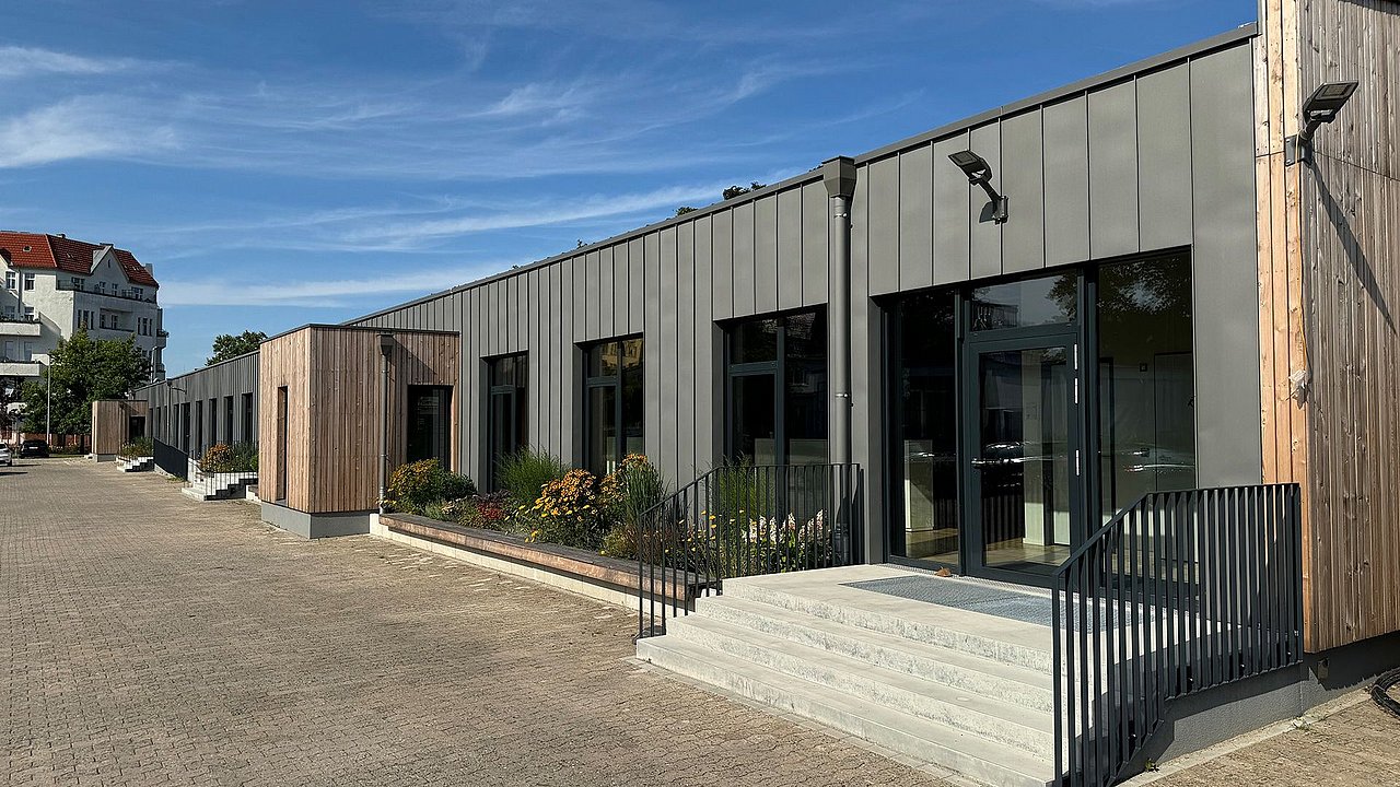 Foto, Modernes, langgestrecktes Gebäude mit grauer Fassade und Holzverkleidung, Treppe mit schwarzem Geländer, blauer Himmel