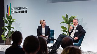 Foto, zwei Menschen sitzen auf einer Bühne und unterhalten sich im Rahmen einer Podiumsdiskussion.