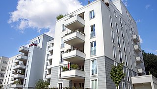 Foto, Mehrstöckiges weißes Wohngebäude mit Balkonen und Pflanzen unter blauem Himmel mit Wolken