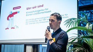 Foto, Mann mit Mikrofon vor Präsentationsfolie.