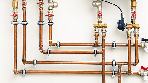 Foto, mehere Kupferleitungen eines Heizungssystems an einer Wand montiert.