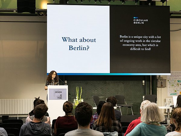 Foto, Rednerin auf einer Bühne vor Publikum