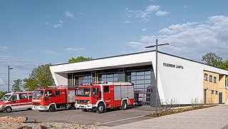 Foto, Neubau einer Feuerwache, vor der Wache geparkt mehrere Feuerwehrfahrzeuge.