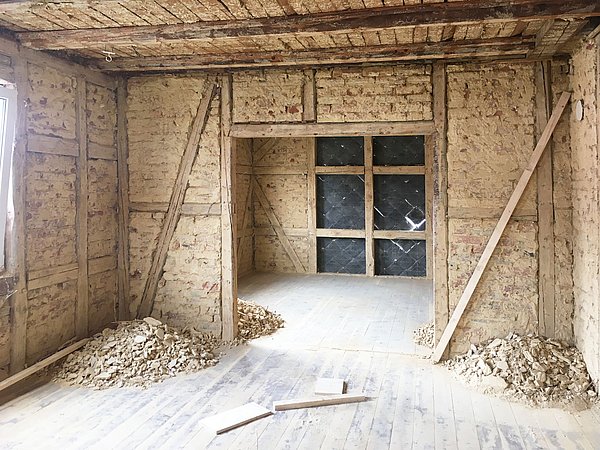 Foto, Innenraum eines alten Fachwerkhauses mit freigelegten Holzbalken und Wänden, Baustellenstaub und Schutt auf dem Boden