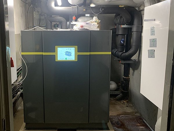 Foto, Große graue Heizungsanlage mit digitalem Display in einem Kellerraum mit Rohren und Beleuchtung