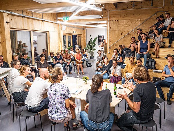 Foto, Gruppe von Menschen um einen Tisch sitzend mit Zuschauern auf Rängen sitzend