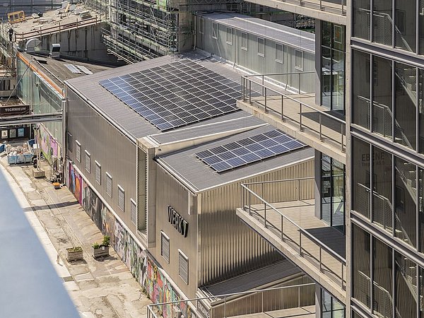 Foto, Blick auf moderne Bürogebäude im Werksviertel Mitte in München mit Solarpaneelen auf dem Dach und Baustelle im Hintergrund