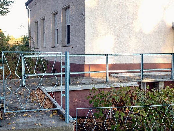 Altes Haus mit verputzter Fassade, erhöhtem Eingang mit Metallgeländer und dekorativem Metalltor, Herbstlaub auf Boden und Terrasse.