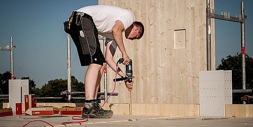 Foto, eine Person in Arbeitskleidung bohrt auf einer Baustelle in den Fußboden.