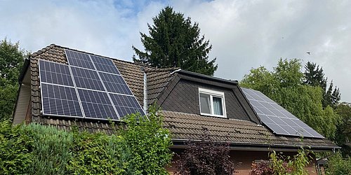 Foto, Dach mit Photovoltaikanlage und Teile der Klinkerfassade eines Einfamilienhauses, das hinter Begrünung steht