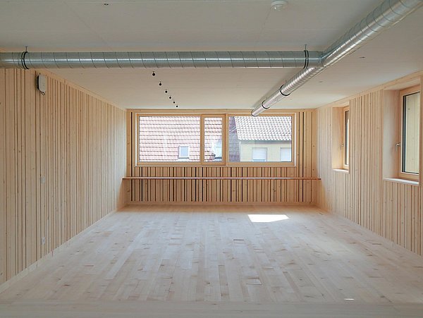 Foto, Innenraum mit Holzboden und Holzverkleidung an den Wänden. An der Decke verlaufen Leitungen. 