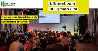 Foto, Menschen sitzen vor einer Bühne, auf der ein Vortrag gehalten wird.