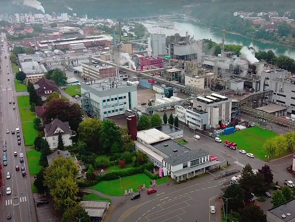Luftaufnahme eines Industriegebiets mit Fabrikgebäuden, Schornsteinen und angrenzenden Straßen neben einem Fluss, aufsteigendem Rauch von industrieller Abwärme.