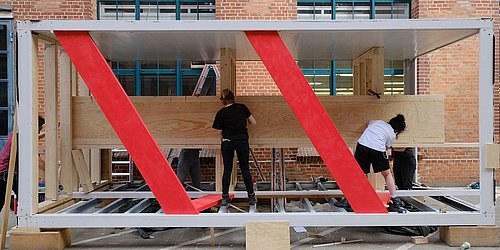 Foto, zwei Personen arbeiten an einer Holzkonstruktion